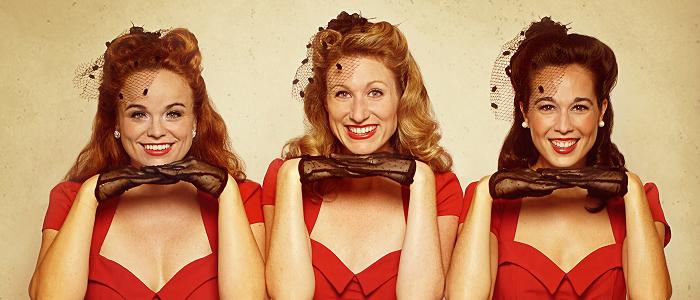 Three women in matching red vintage-style dresses and black gloves smiling and posing together