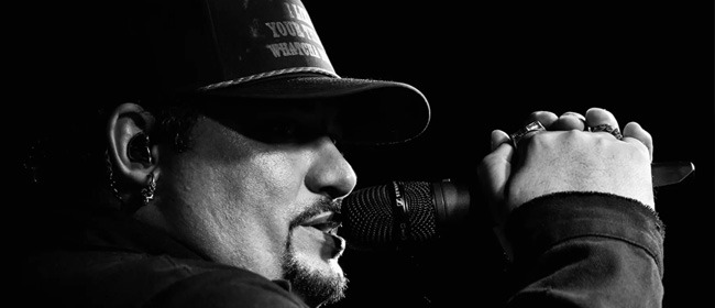 Man with goatee and a ballcap sings into a microphone