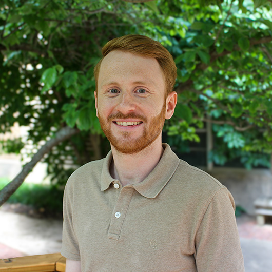 Smiling man in grey polo, with red hair and beard.