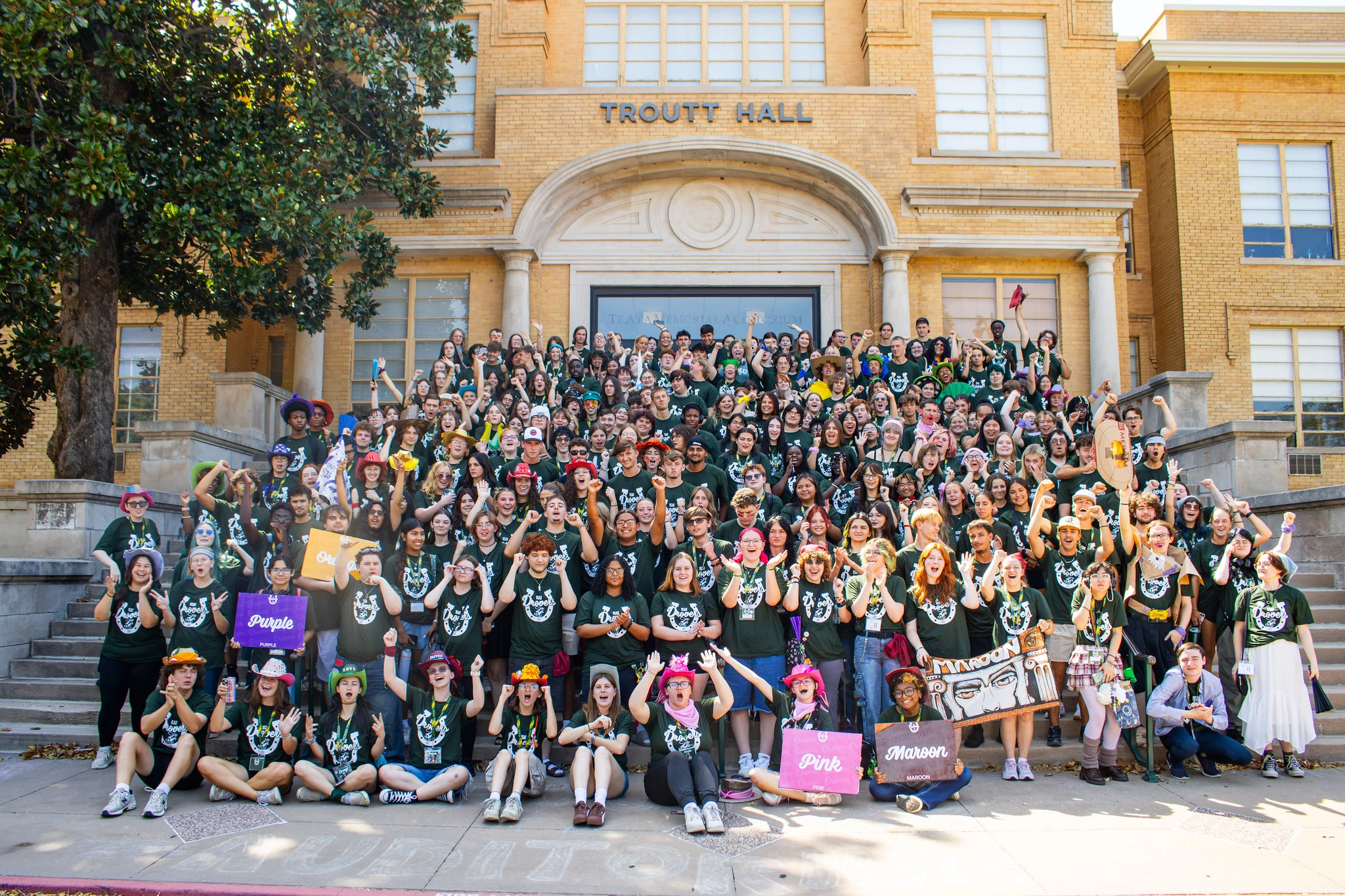Large group of USAO students gathers on the steps of Troutt Hall, cheering and posing for a photograph.